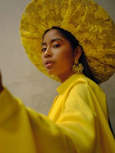 a woman wearing a yellow hat and holding her hand up to the side with one hand