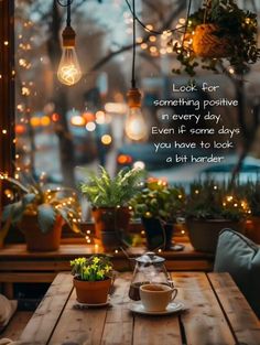 a wooden table topped with two cups of coffee next to potted plants and lights