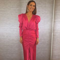 a woman standing in front of a wall wearing a pink dress