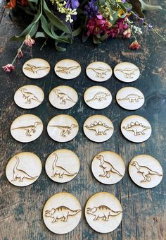 twelve wooden dinosaur coasters sitting on a table next to flowers and purple pansies