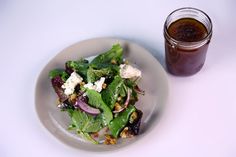 a white plate topped with salad next to a jar of dressing