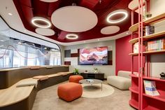 the interior of a modern office with red and white walls, circular lights, bookshelves, and chairs