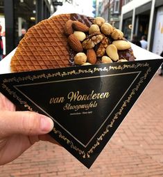 a person holding up a waffle with nuts and chocolate on it in front of a building