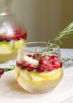 two glasses filled with drinks and garnished with cranberries on a table