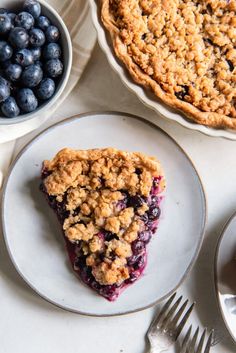 a slice of blueberry crumb pie on a plate next to two bowls of berries