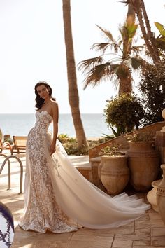 a woman in a wedding dress standing on a patio next to palm trees and the ocean