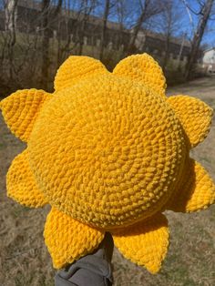 a person wearing a yellow crocheted sunflower hat in front of some trees