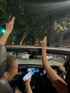 two people in a car holding up their cell phones while driving down the street at night