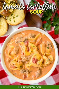 a white bowl filled with pasta and meat soup next to bread on a red checkered tablecloth