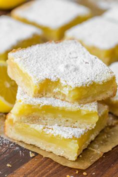 three lemon bars stacked on top of each other with powdered sugar and two lemons in the background