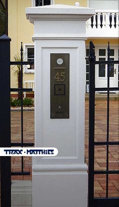 a tall white clock sitting in the middle of a sidewalk next to a black fence