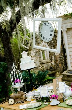 a table topped with lots of plates covered in cake next to a clock and birdcage