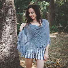 a woman standing next to a tree wearing a blue and white ponched top