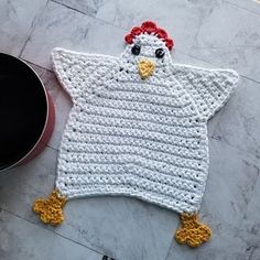 a crocheted chicken is laying on the floor next to a pot holder and pan