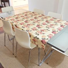 a dining room table covered with a flowered table cloth and four white chairs in front of it