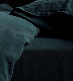 an unmade bed with dark green sheets and pillows