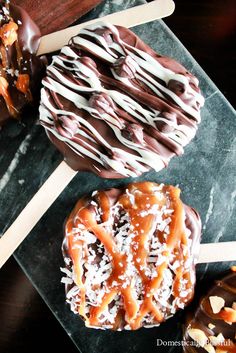 three chocolate covered donuts sitting on top of a black plate next to two popsicle sticks