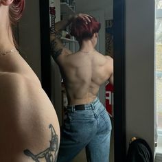 a woman with red hair is looking at herself in the mirror and has tattoos on her back