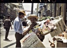 two men are standing on the street with newspapers in their hands and one man is wearing a straw hat