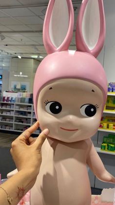 a person touching the face of a stuffed animal wearing a pink bunny hat in a store