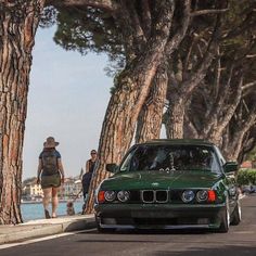 a green car parked on the side of a road next to some trees and people