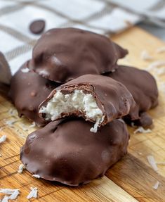 three chocolate covered donuts on a wooden cutting board with coconut flakes around them