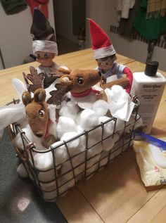 two elfs are sitting in a basket filled with cotton balls and stuffed reindeer heads