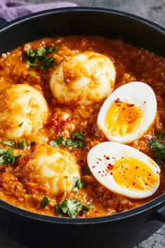 three eggs are in a skillet with red sauce and parsley on the side