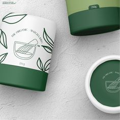 two green cups sitting next to each other on top of a white wall with leaves