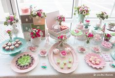 a table topped with lots of cakes and cupcakes next to a window filled with flowers