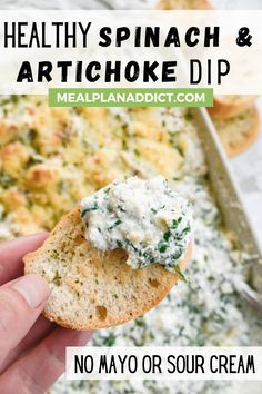 a hand holding a cracker with spinach and artichoke dip on it