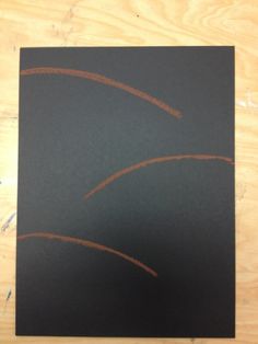 a piece of black paper that has some brown lines on it and is sitting on top of a wooden table