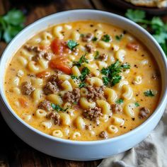 a white bowl filled with pasta and meat soup on top of a wooden table next to bread