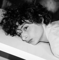 a black and white photo of a woman with curly hair laying down on a table