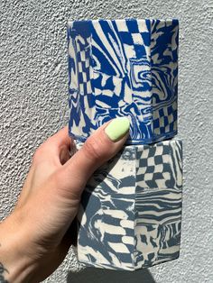 a woman's hand holding a blue and white patterned cup with green nail polish