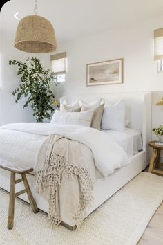 a bed with white linens and pillows in a bedroom next to a plant hanging from the ceiling