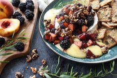 a plate filled with fruit and crackers on top of a wooden cutting board next to sliced peaches