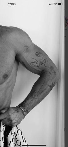 a shirtless man with tattoos on his arm and chest standing in front of a white wall