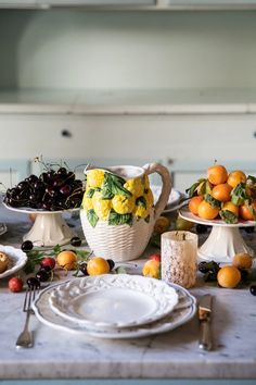 the table is set with plates and bowls of fruit, including oranges, cherries, lemons, and plums