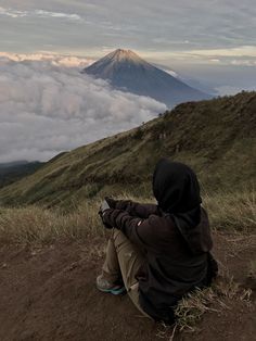 a person sitting on top of a hill looking at the clouds and mountains in the distance