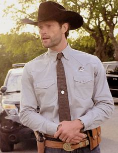 a man wearing a cowboy hat standing in front of a truck with his hands in his pockets