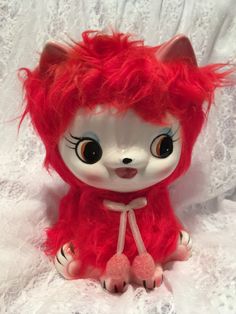 a red and white stuffed animal sitting on top of a white bed sheet with lace