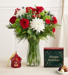 a glass vase filled with red and white flowers next to a small house shaped box