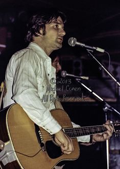 a man holding a guitar while standing in front of a microphone and singing into a microphone