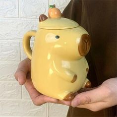 a person holding a yellow ceramic teapot with an animal on it's lid