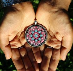 two hands are holding a pink and blue brooch