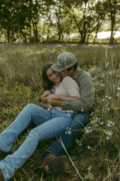 a man and woman sitting on the ground in a field with wildflowers behind them