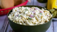 a green bowl filled with macaroni salad next to some pickles and bread