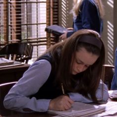 a woman sitting at a table writing on a piece of paper with a pencil in her hand