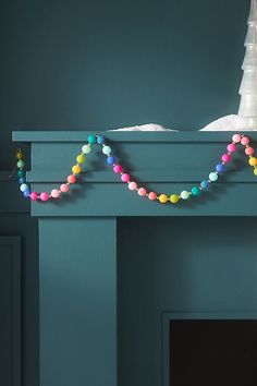 a fireplace mantel decorated with multicolored beads and a white christmas tree in the background